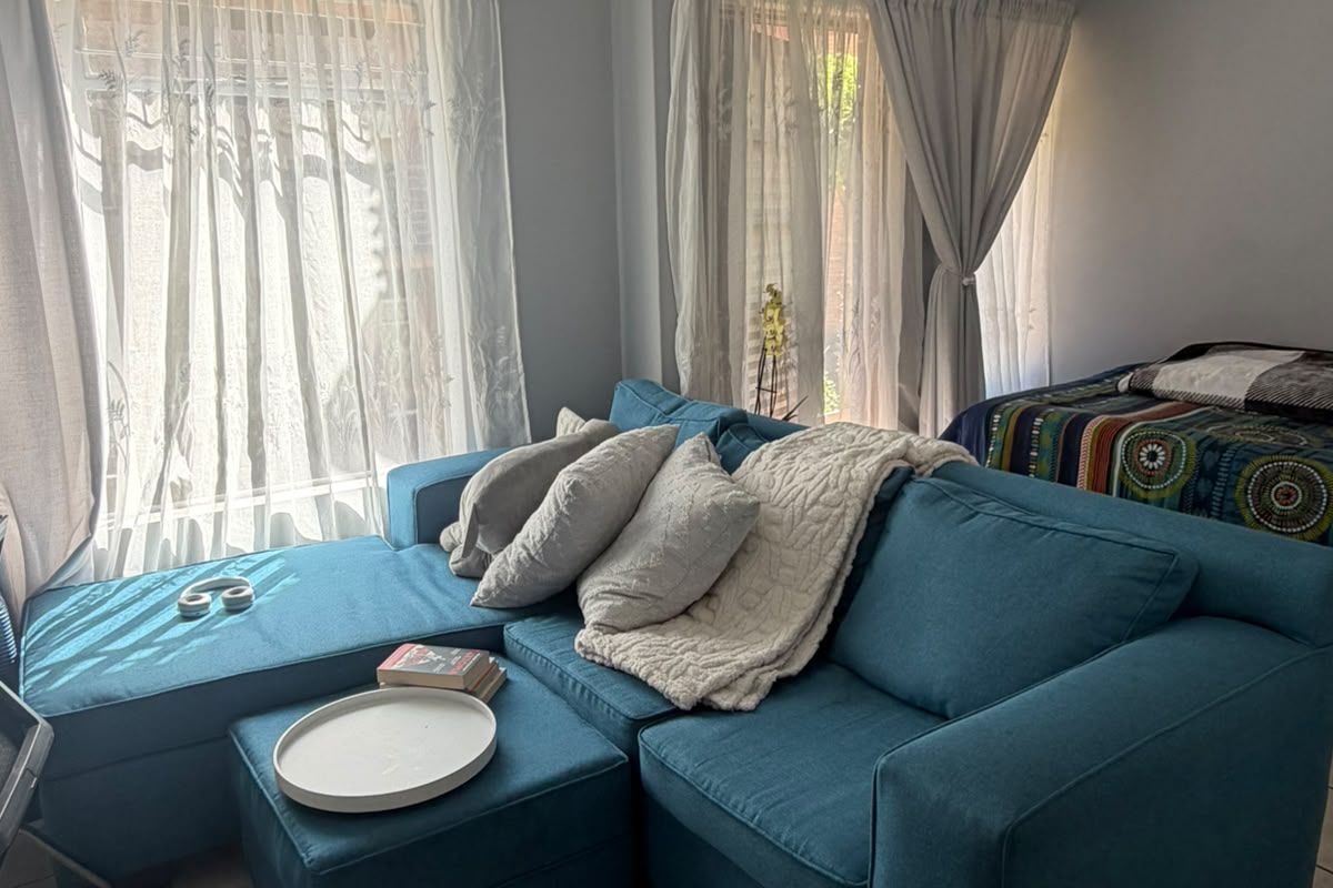 A living room area featuring tiled flooring and natural light from dual windows, providing a functional space for relaxation.