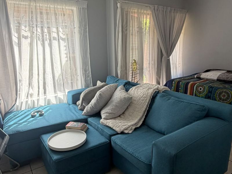 A living room area featuring tiled flooring and natural light from dual windows, providing a functional space for relaxation.
