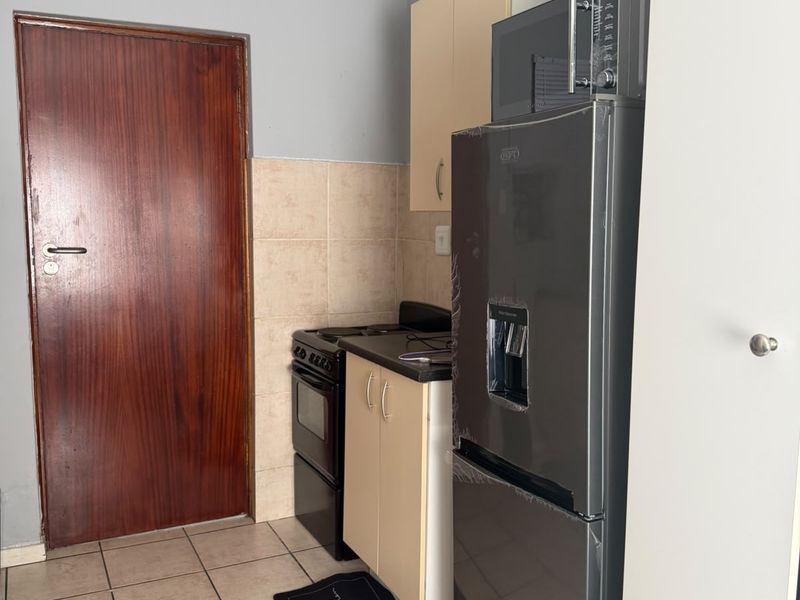 A compact kitchen featuring tiled flooring, a tiled backsplash, built-in cabinetry, and a freestanding stove.