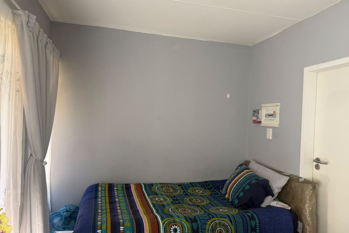 A simple bedroom featuring grey walls, a curtain rail, and a wall-mounted electrical distribution board with a prepaid meter.