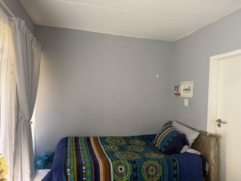 A simple bedroom featuring grey walls, a curtain rail, and a wall-mounted electrical distribution board with a prepaid meter.