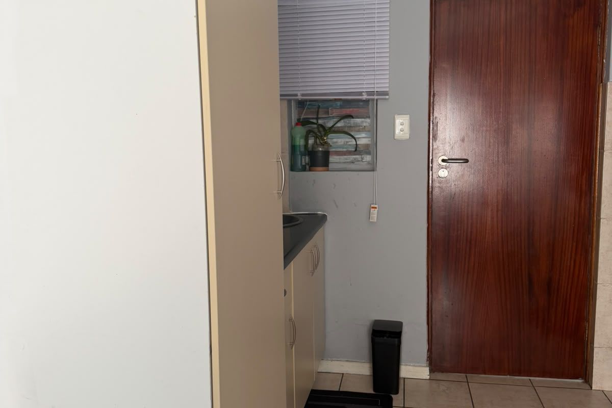 A compact kitchen area featuring built-in cabinetry, tiled flooring, and a solid wood door, offering a functional layout in need of cosmetic updates.