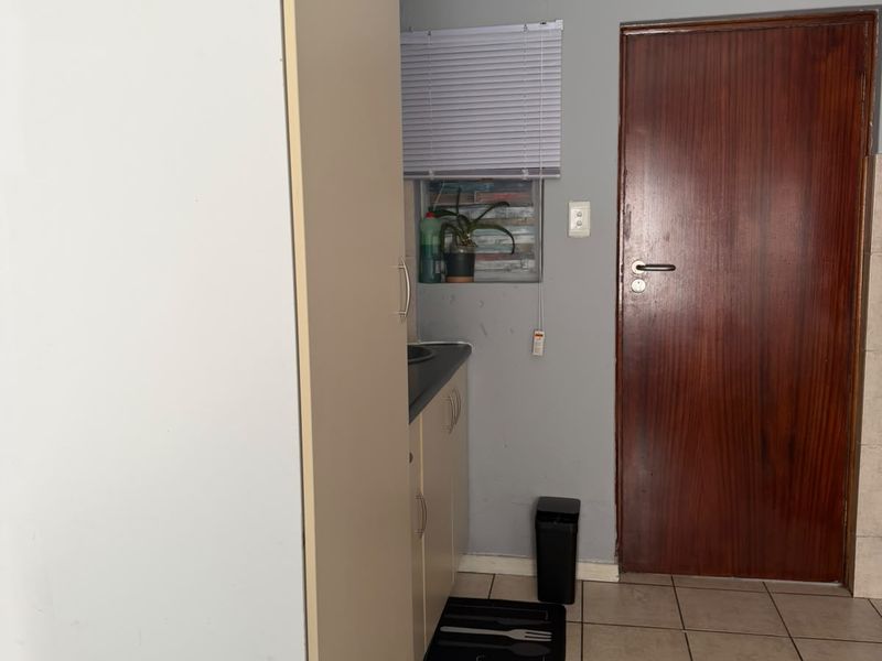 A compact kitchen area featuring built-in cabinetry, tiled flooring, and a solid wood door, offering a functional layout in need of cosmetic updates.