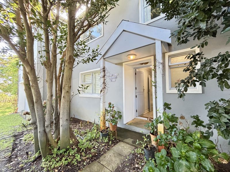 Front entrance of the house featuring a covered porch, paved walkway, and established garden surroundings.