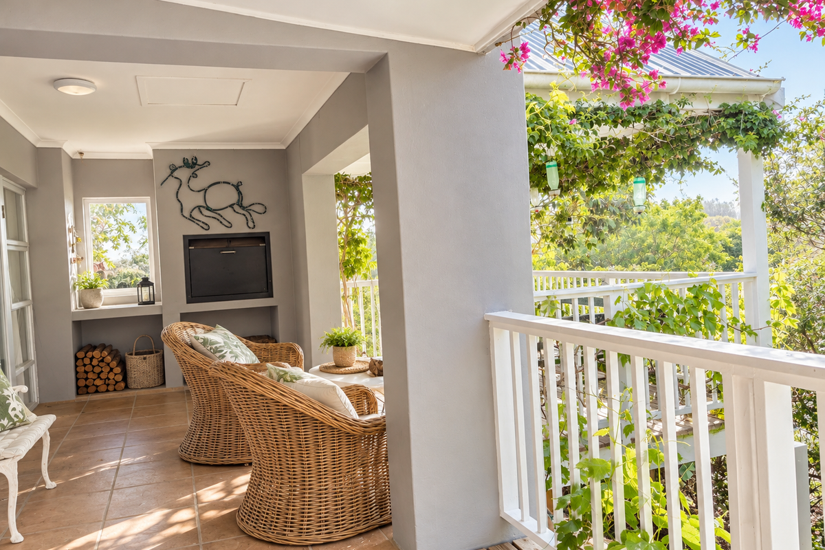 A covered patio featuring a built-in fireplace, tiled flooring, and a white balustrade overlooking a lush garden area.