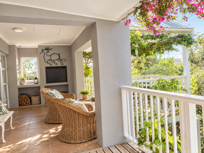 A covered patio featuring a built-in fireplace, tiled flooring, and a white balustrade overlooking a lush garden area.