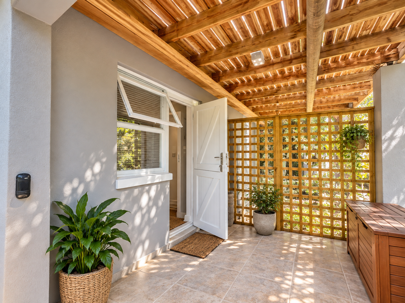 A well-maintained covered patio featuring a timber pergola, tiled flooring, and a decorative lattice screen, providing a pleasant outdoor transition space.