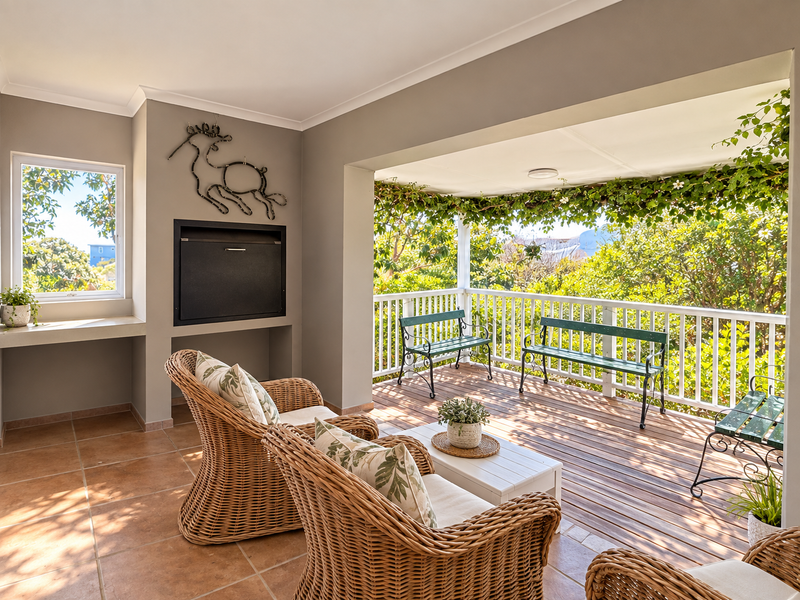 A spacious covered patio featuring a built-in braai, wooden decking, and a secure railing, offering a pleasant outdoor living and entertainment area.