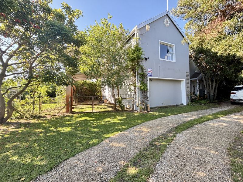 Front exterior view of the property featuring a gravel driveway, garage access, and established garden surroundings.