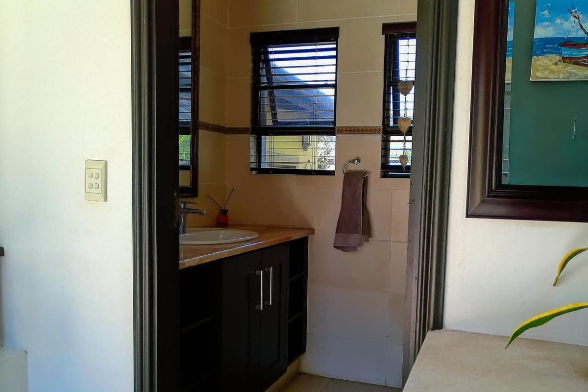 A functional bathroom featuring a dark wood vanity cabinet, integrated basin, and tiled wall finishes with louvered windows for natural ventilation.