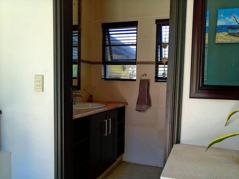 A functional bathroom featuring a dark wood vanity cabinet, integrated basin, and tiled wall finishes with louvered windows for natural ventilation.