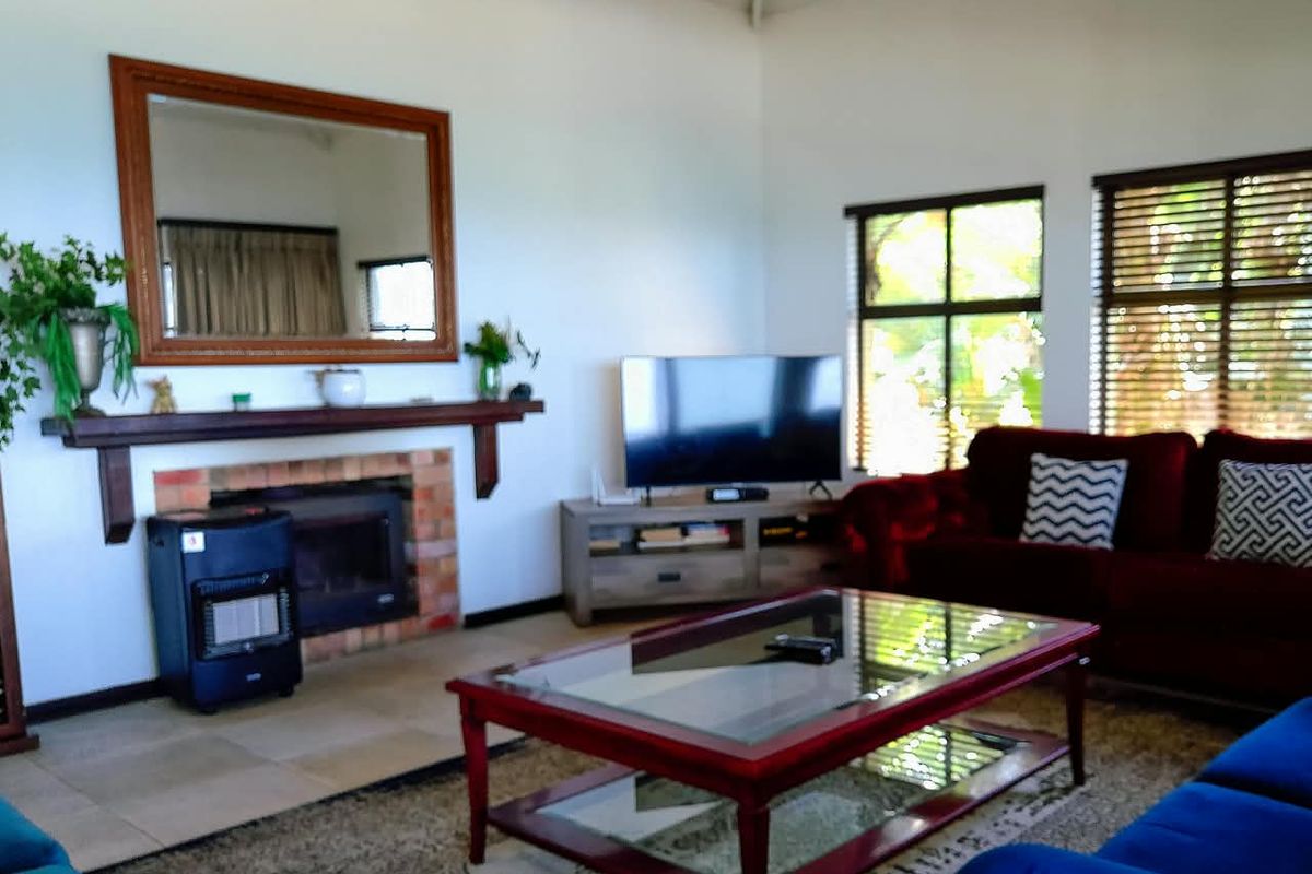 A comfortable living room featuring a brick fireplace with a wooden mantelpiece, large windows with venetian blinds, and high ceilings.