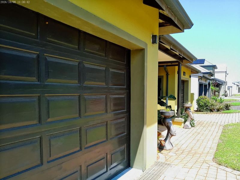 A view of the front exterior featuring a dark sectional garage door, paved driveway, and yellow painted facade.