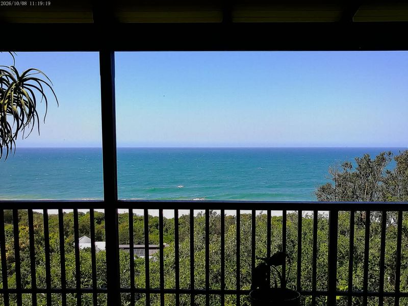 A covered balcony offering expansive, elevated views of the ocean and surrounding coastal vegetation.