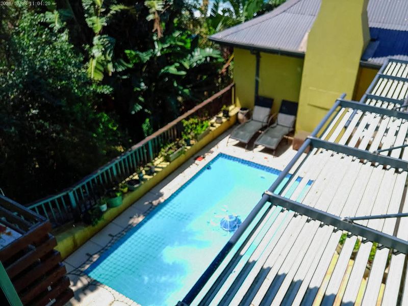 An elevated view of a rectangular swimming pool with a pergola structure and surrounding garden area.