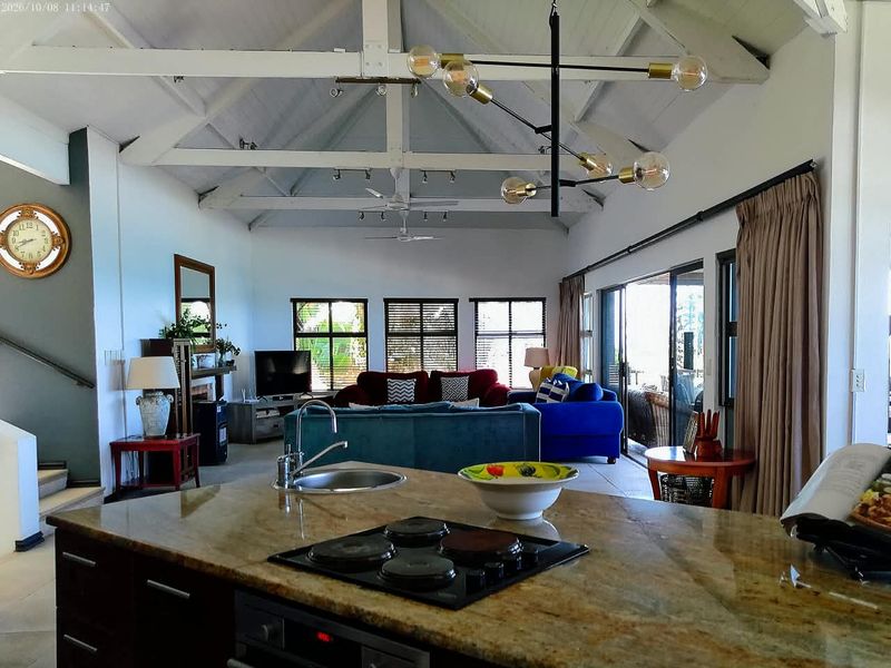 Spacious open-plan living area featuring a kitchen island with granite countertops, vaulted ceilings with exposed timber trusses, and large sliding doors leading outdoors.