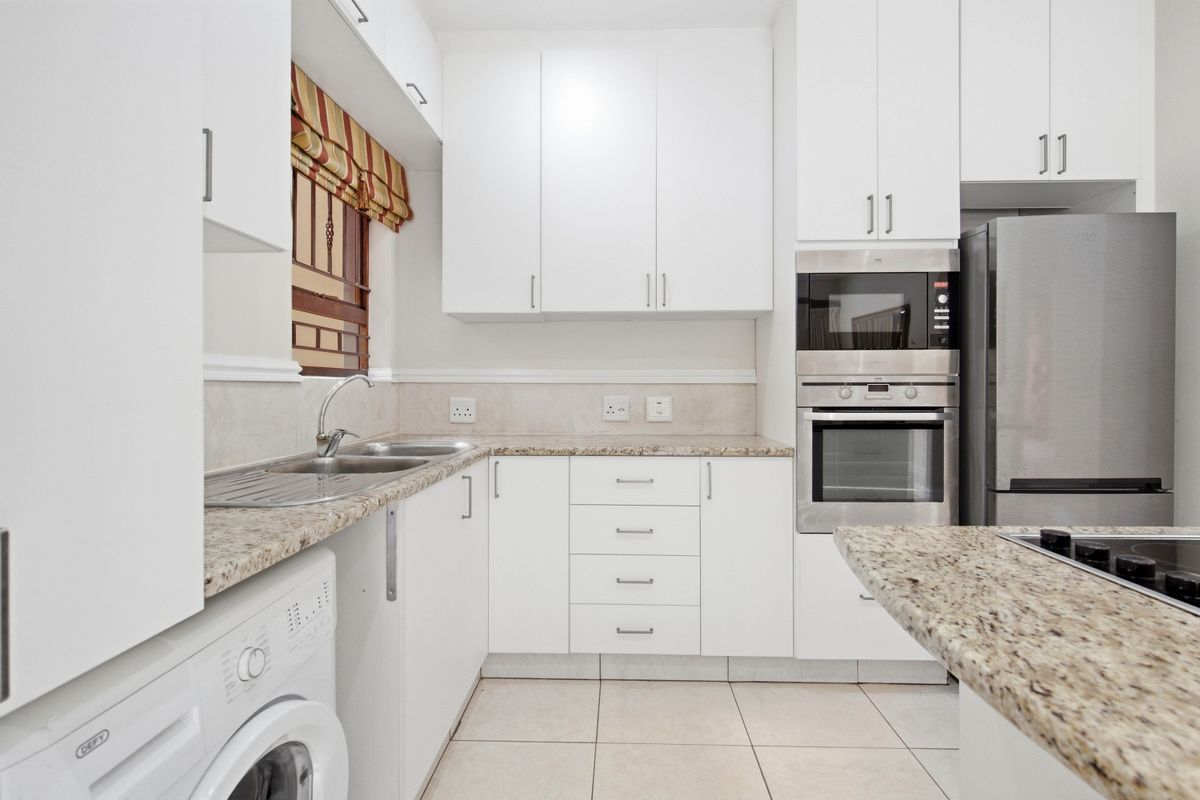 Modern kitchen featuring white cabinetry, granite countertops, built-in oven, microwave, and hob, with tiled flooring and a stainless steel sink.