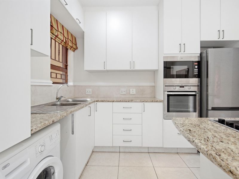 Modern kitchen featuring white cabinetry, granite countertops, built-in oven, microwave, and hob, with tiled flooring and a stainless steel sink.