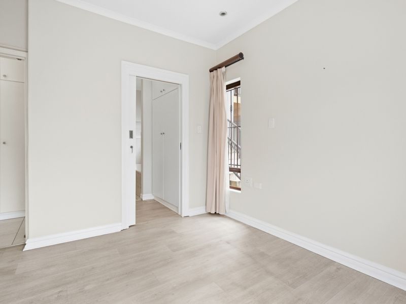 A bright, empty bedroom featuring neutral walls, light laminate flooring, and built-in cupboards, offering a clean and versatile space.