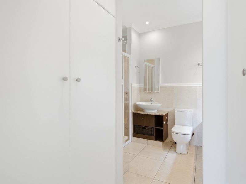 A clean and well-maintained bathroom featuring a vessel sink vanity, toilet, shower enclosure, and ample built-in storage cupboards.