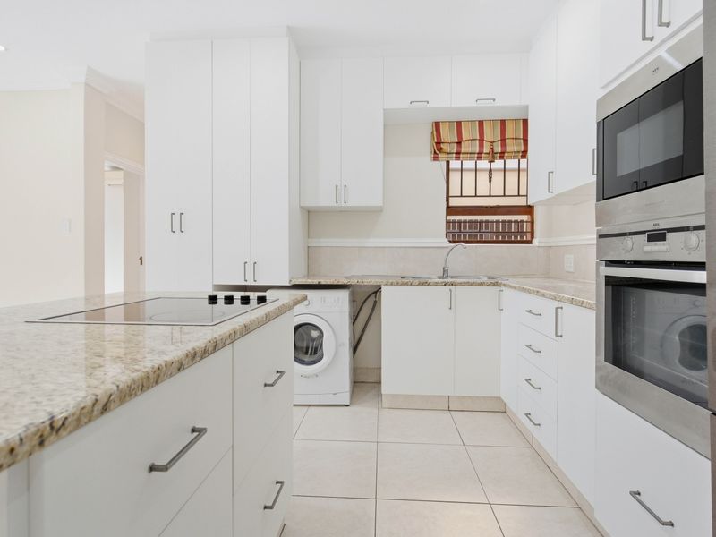 Modern kitchen featuring white cabinetry, granite countertops, built-in oven and microwave, electric cooktop, and tiled flooring with integrated laundry space.