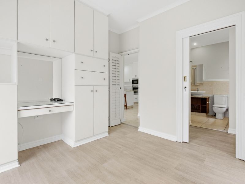 A bright bedroom featuring extensive built-in cabinetry with an integrated vanity desk, light laminate flooring, and direct access to an adjoining bathroom.