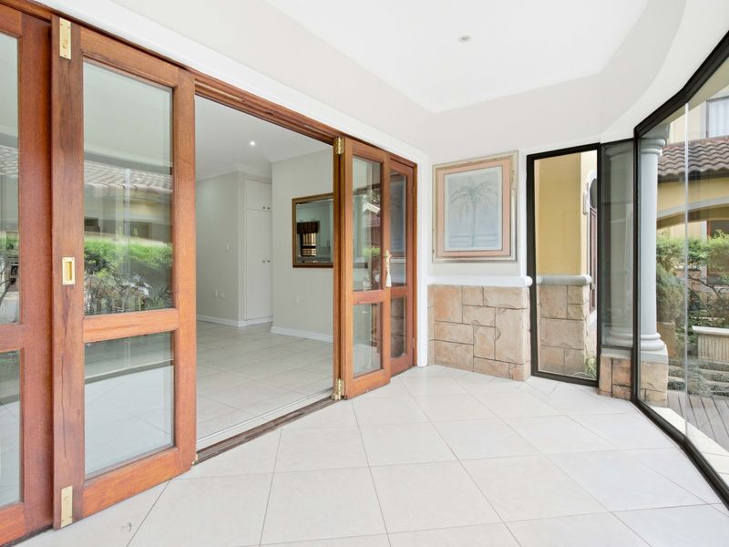 A bright, covered patio area featuring tiled flooring, stone cladding accents, and large wooden sliding doors that open into the interior living space.