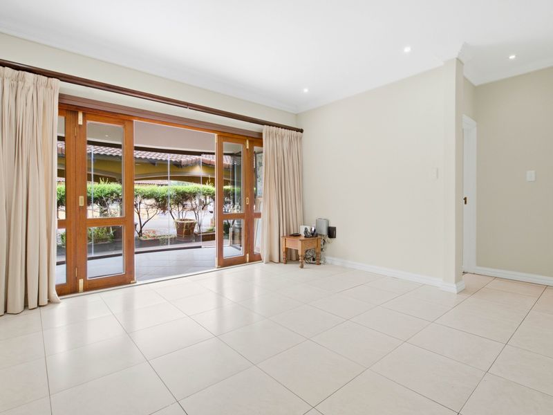 Spacious, light-filled living area featuring neutral tiled flooring, recessed downlighting, and large wooden sliding doors opening onto a covered patio.