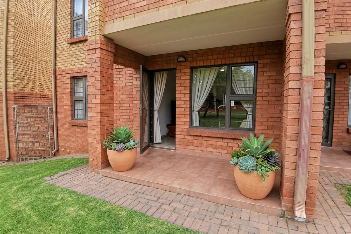 A covered brick patio area with tiled flooring, providing direct access to the interior through a glass door and window.