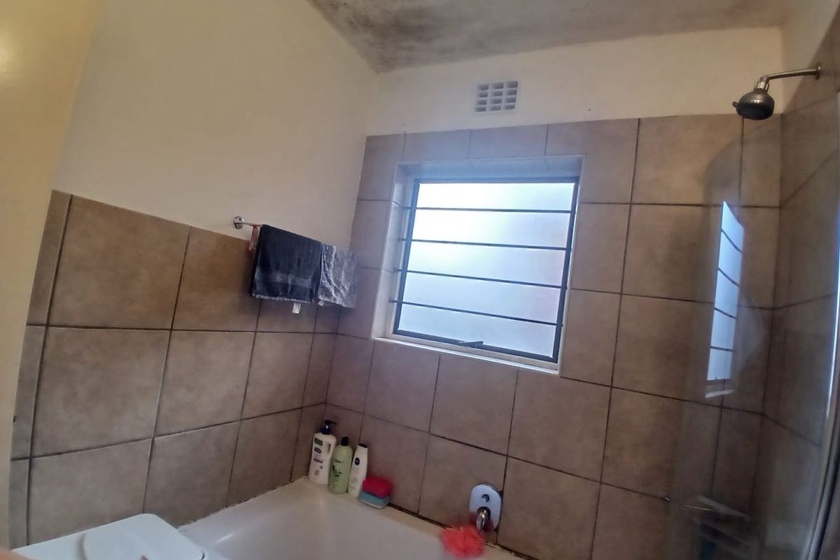 A functional bathroom featuring a bathtub with shower head, tiled walls, and a window with security bars, currently showing signs of ceiling moisture damage.