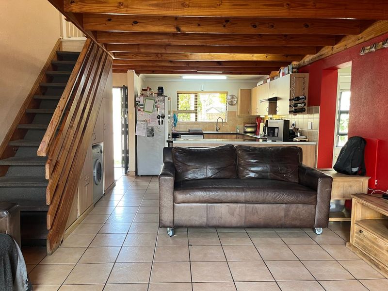 Open-plan living area featuring exposed timber ceiling beams, tiled flooring, a wooden staircase with integrated storage, and a functional kitchen layout.