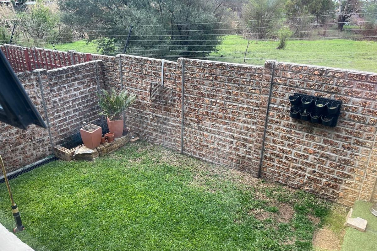 A private rear garden featuring a small lawn area enclosed by a precast concrete boundary wall with integrated electric fencing.