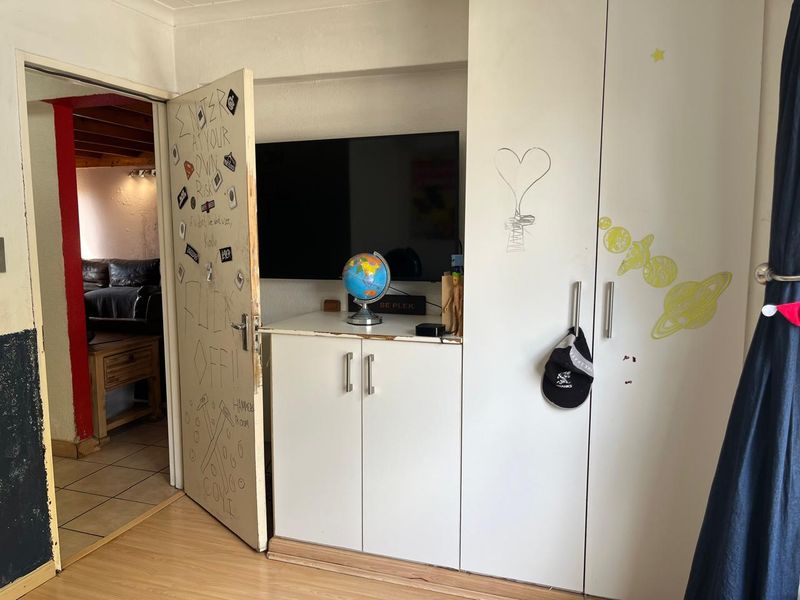 Bedroom featuring built-in cupboards and laminate flooring, currently showing signs of wear and surface damage requiring cosmetic attention.