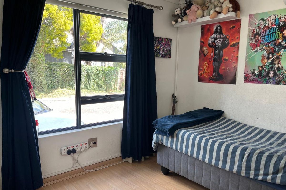 A bedroom featuring laminate flooring and a large aluminium-framed window, providing natural light and a view of the street.