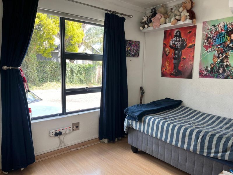 A bedroom featuring laminate flooring and a large aluminium-framed window, providing natural light and a view of the street.