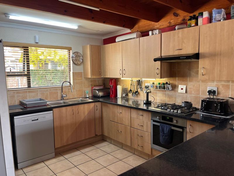 Functional kitchen featuring light wood cabinetry, granite countertops, gas hob, built-in oven, and exposed timber ceiling beams with tiled flooring.