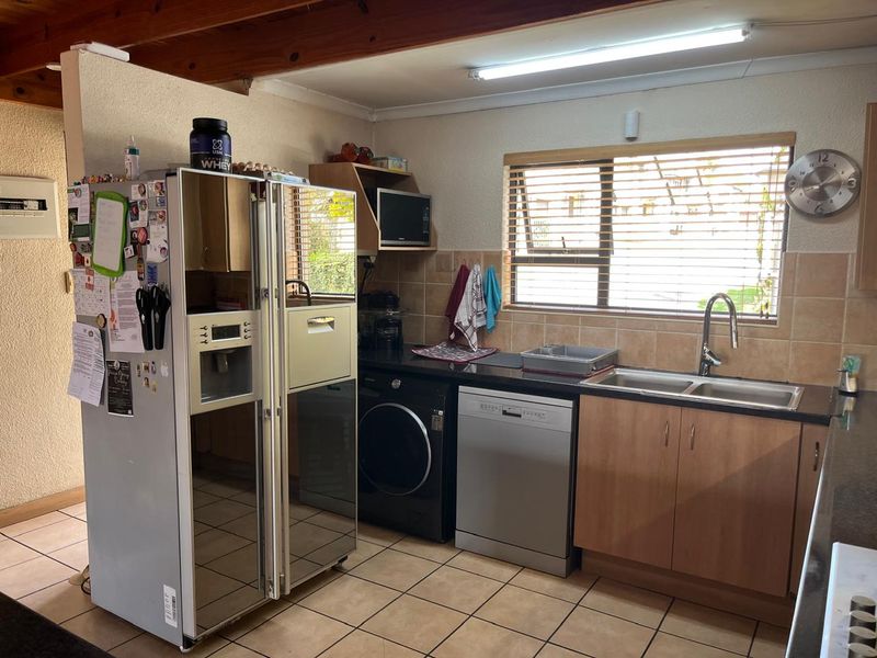 Functional kitchen featuring built-in cabinetry, double sink, tiled backsplash, and exposed timber ceiling beams, offering a practical layout with integrated appliance spaces.