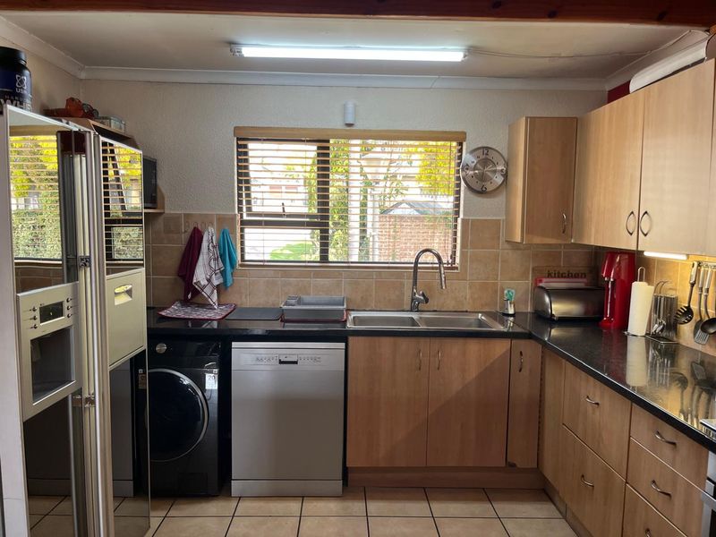 A functional kitchen featuring light wood cabinetry, dark laminate countertops, a double sink, and tiled flooring with space for integrated appliances.