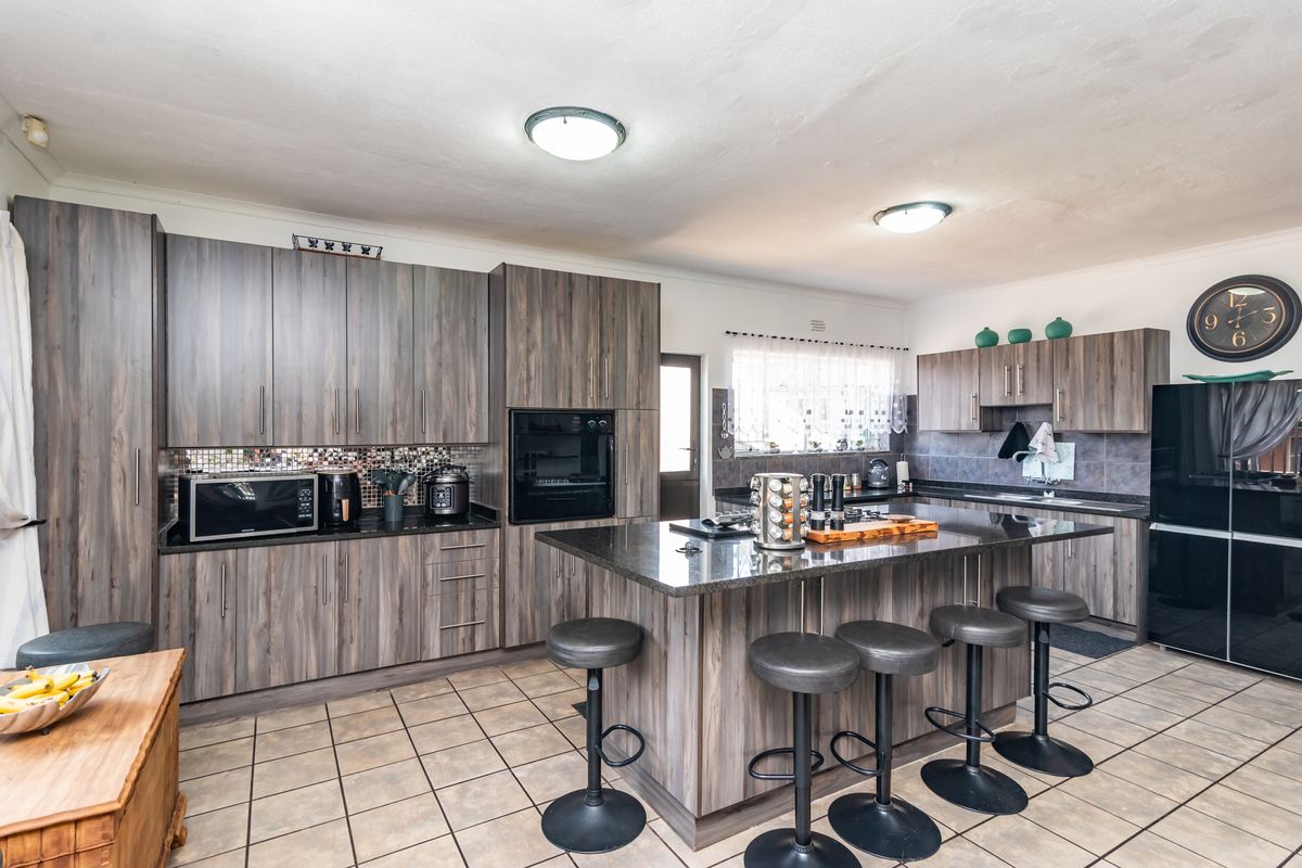 Modern kitchen featuring dark wood-grain cabinetry, granite countertops, a central island with breakfast bar seating, and integrated oven.