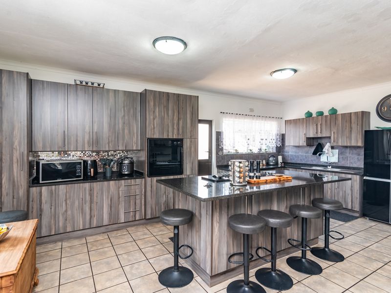 Modern kitchen featuring dark wood-grain cabinetry, granite countertops, a central island with breakfast bar seating, and integrated oven.