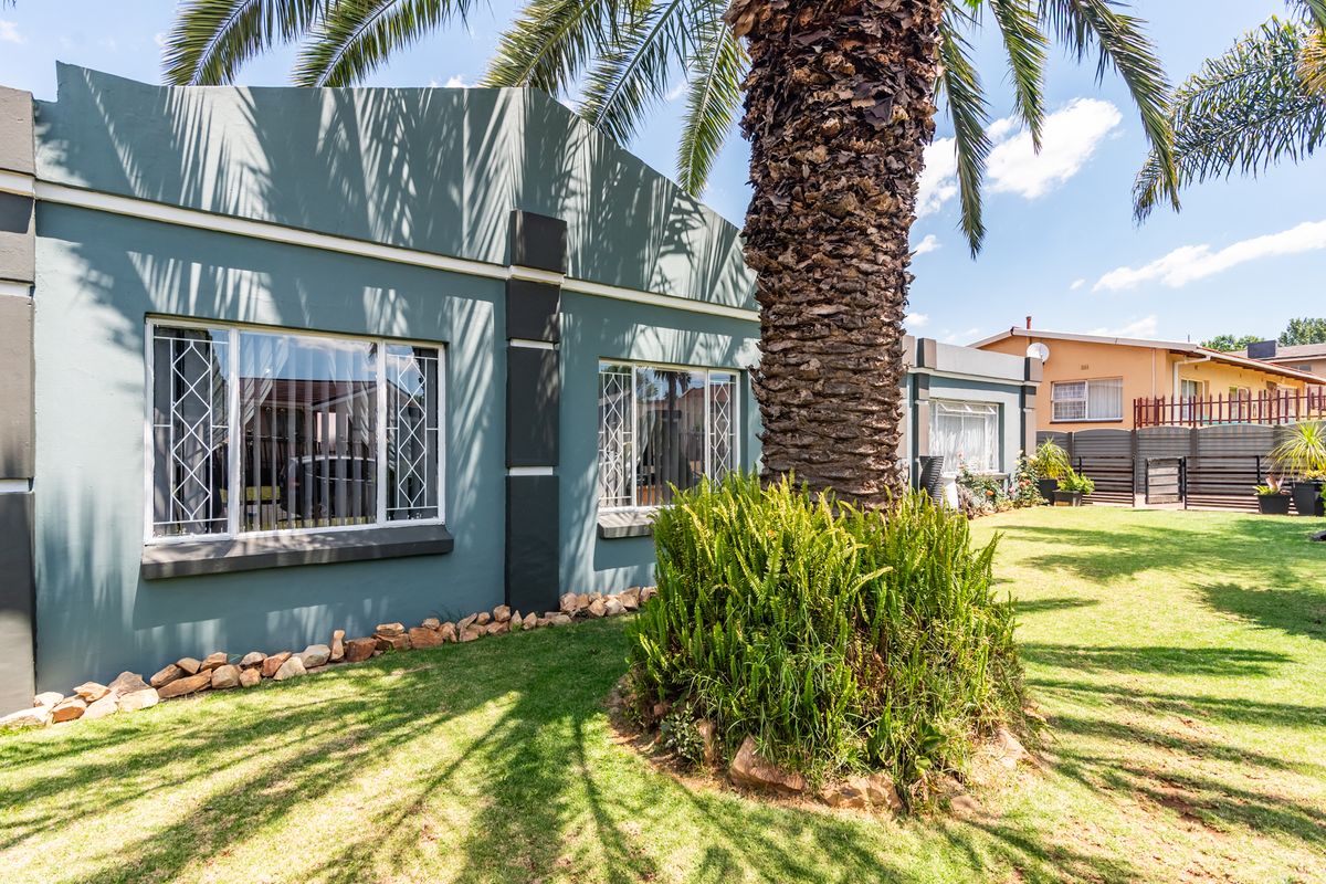 A well-maintained rear exterior view of the house featuring a landscaped garden, mature palm tree, and secure window treatments.
