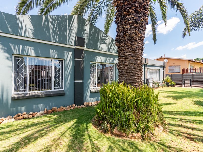 A well-maintained rear exterior view of the house featuring a landscaped garden, mature palm tree, and secure window treatments.