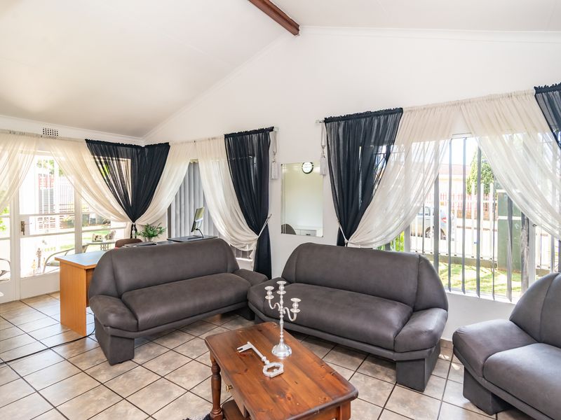 Spacious living room featuring vaulted ceilings, tiled flooring, and large windows with security bars, offering a bright and open atmosphere.