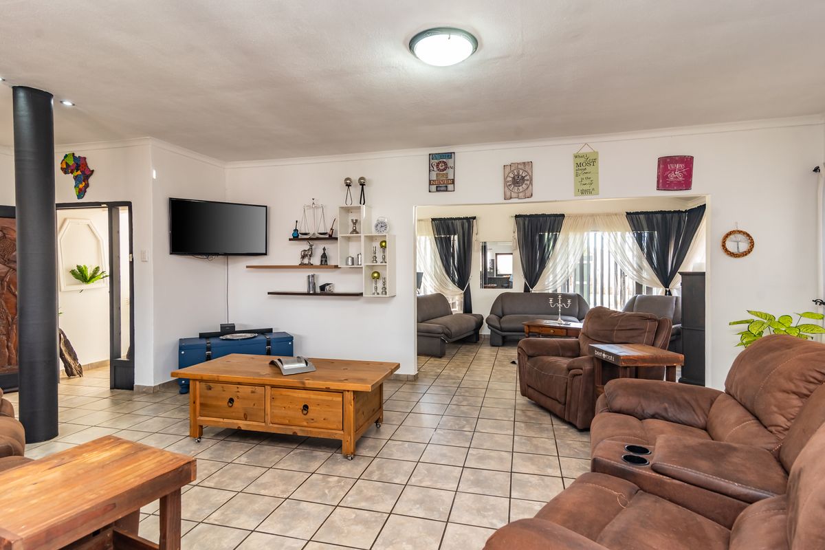 Spacious living area featuring tiled flooring, a central support column, and an open-plan layout connecting to an adjacent lounge space.