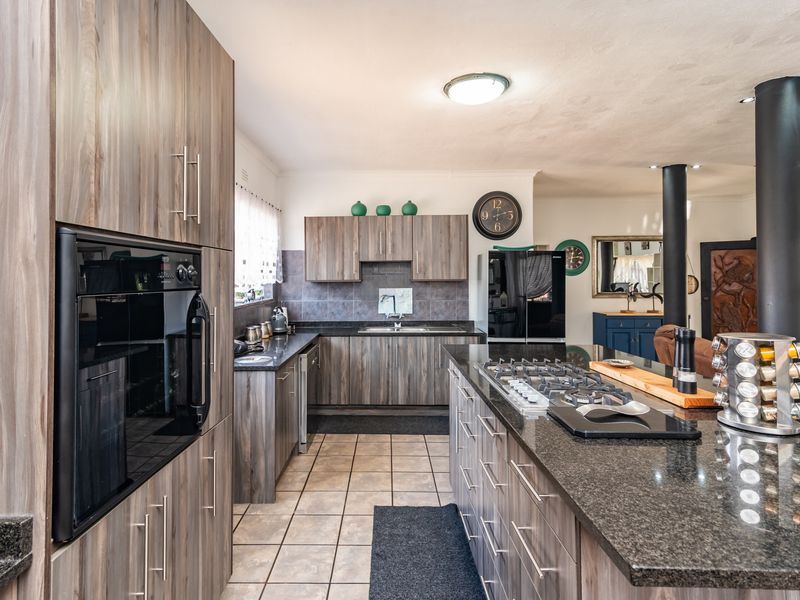 Modern kitchen featuring dark wood-look cabinetry, granite countertops, a central island with a gas hob, and integrated oven, offering a functional and stylish workspace.