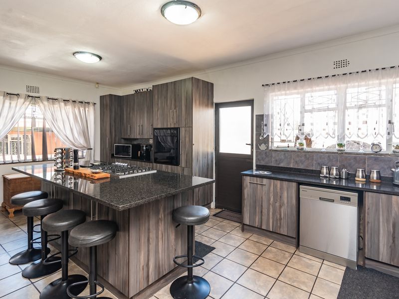 Modern kitchen featuring dark wood cabinetry, granite countertops, a central island with a gas hob, and tiled flooring with ample natural light.
