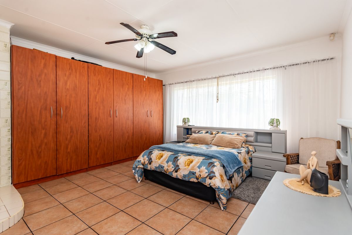 Spacious bedroom featuring large built-in wooden cupboards, tiled flooring, and a ceiling fan, offering a functional layout with ample storage space.