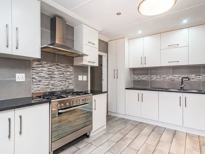 Modern kitchen featuring white cabinetry, stone countertops, a gas stove with extractor fan, and stylish mosaic tile backsplash with neutral floor tiles.