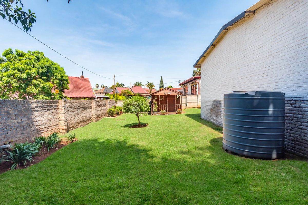A spacious rear garden featuring a lawn, a brick boundary wall, and a large water storage tank against the side of the house.