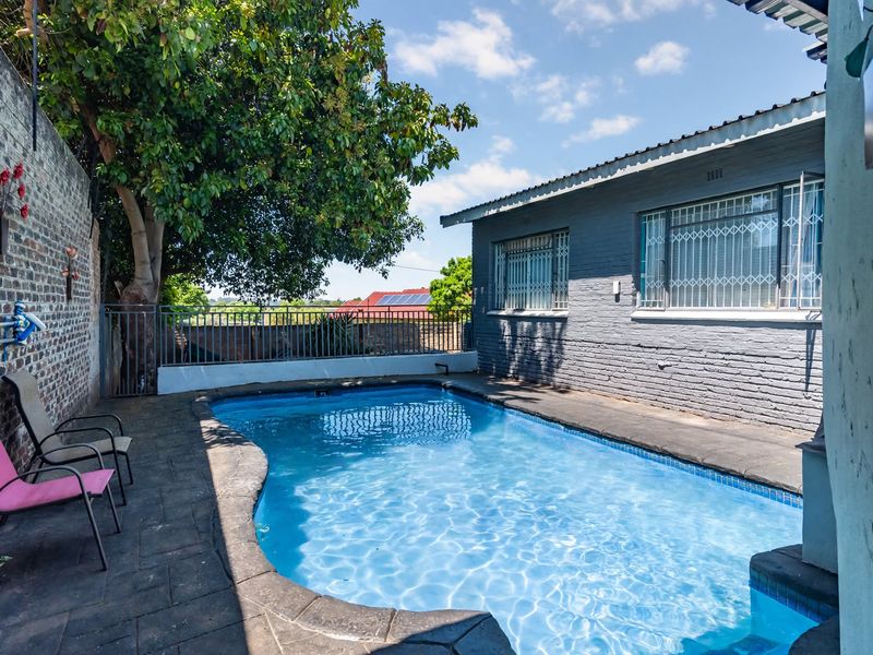 Outdoor pool area featuring a swimming pool, paved surround, and secure boundary walling, set against the painted brick exterior of the house.